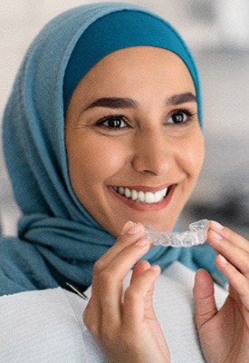 Woman smiling while holding clear aligner in treatment room